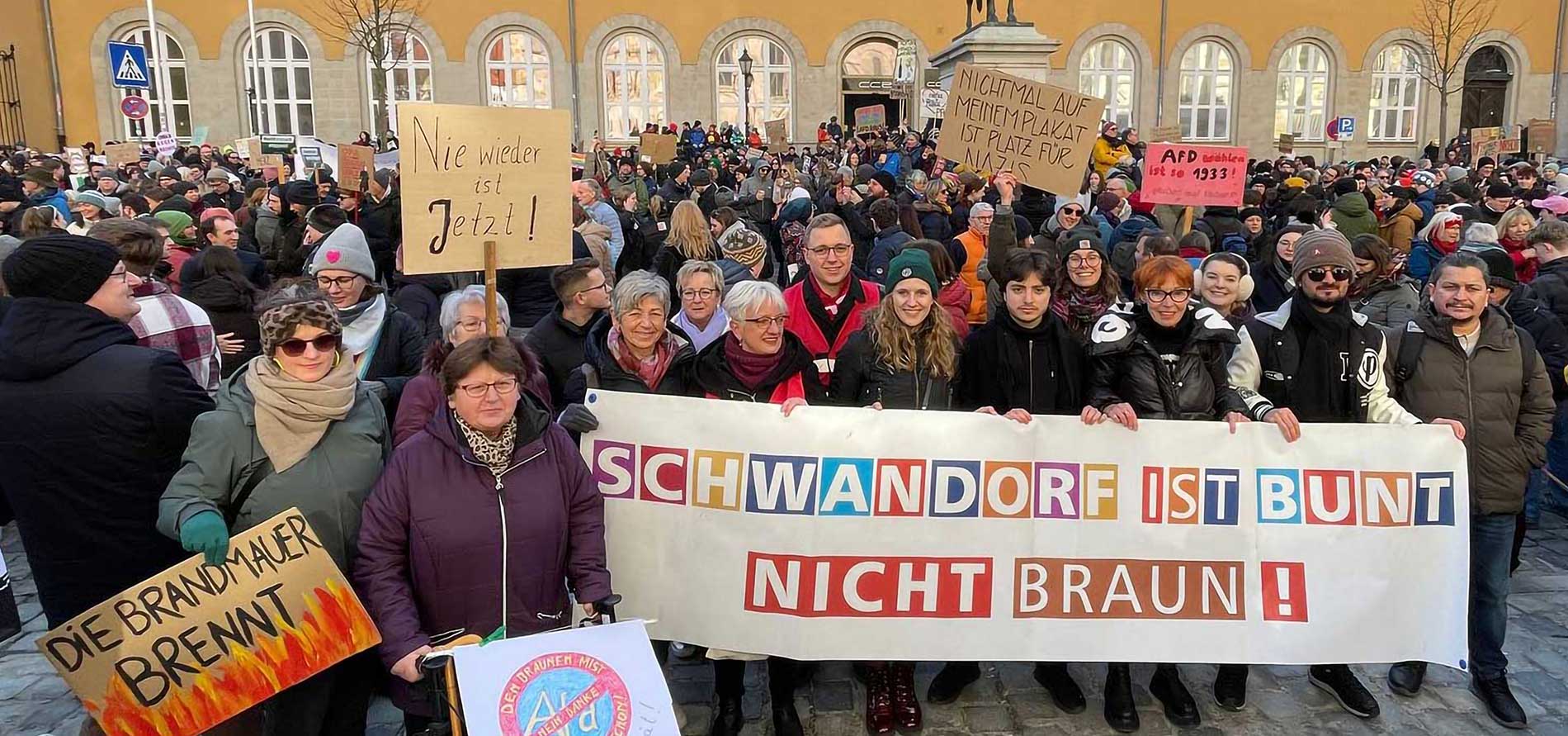 Eine Gruppe des Schwandorfer Bündnisses gegen Rechtsextremismus auf der Großdemonstration gegen die Rechte Normalisierung am 2.2.2025 auf dem Domplatz in Regensburg. Sie stehen hinter dem großen Transparent "Schwandorf ist bunt nicht braun!" und halten Schilder wie "Die Brandmauer brennt".