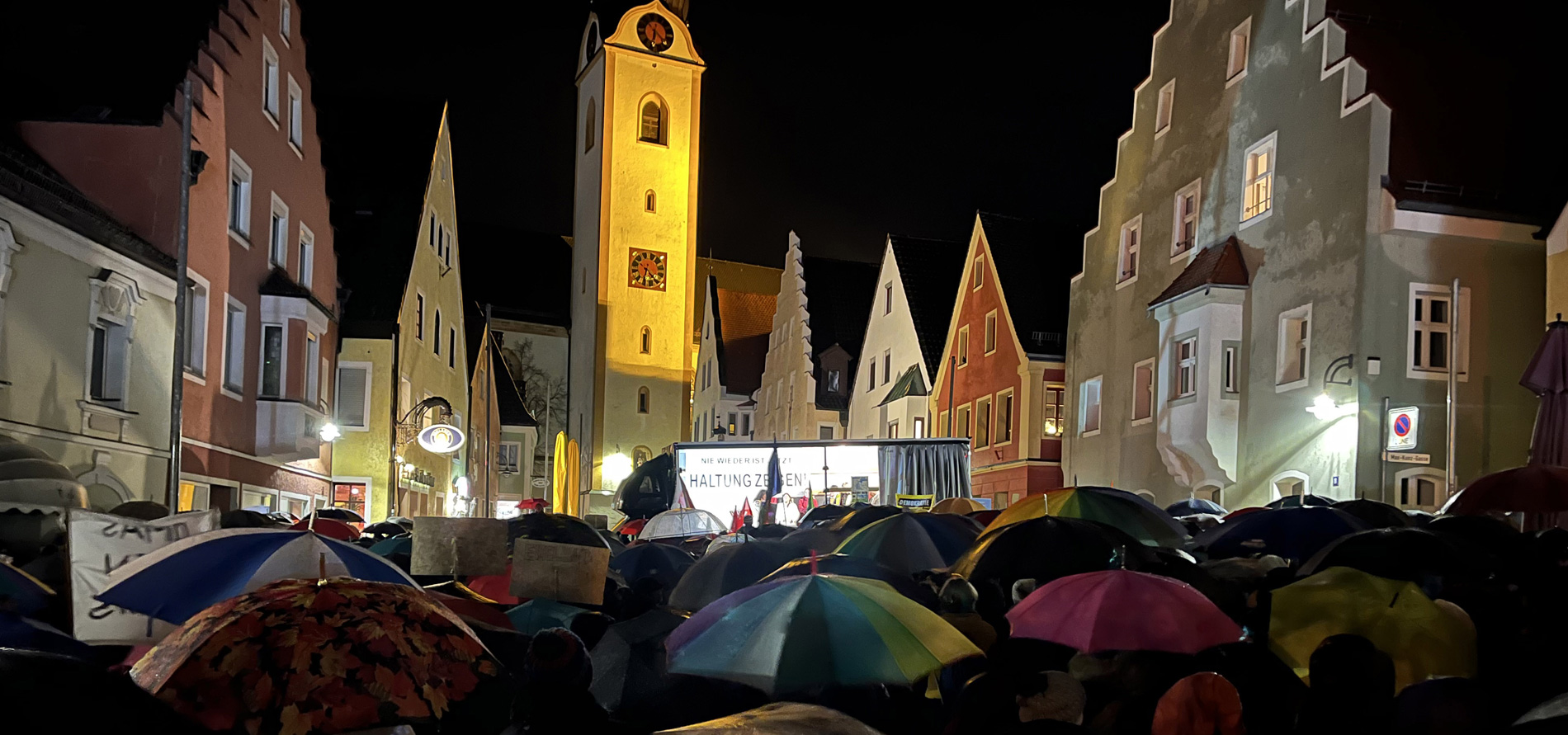 Große Menschenmenge mit vielen Regenschirmen bei Nacht auf dem Marktplatz von Schwandorf. Im Hintergrund der angestrahlte Kirchturm.